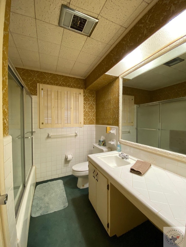 full bathroom with combined bath / shower with glass door, toilet, vanity, and tile walls