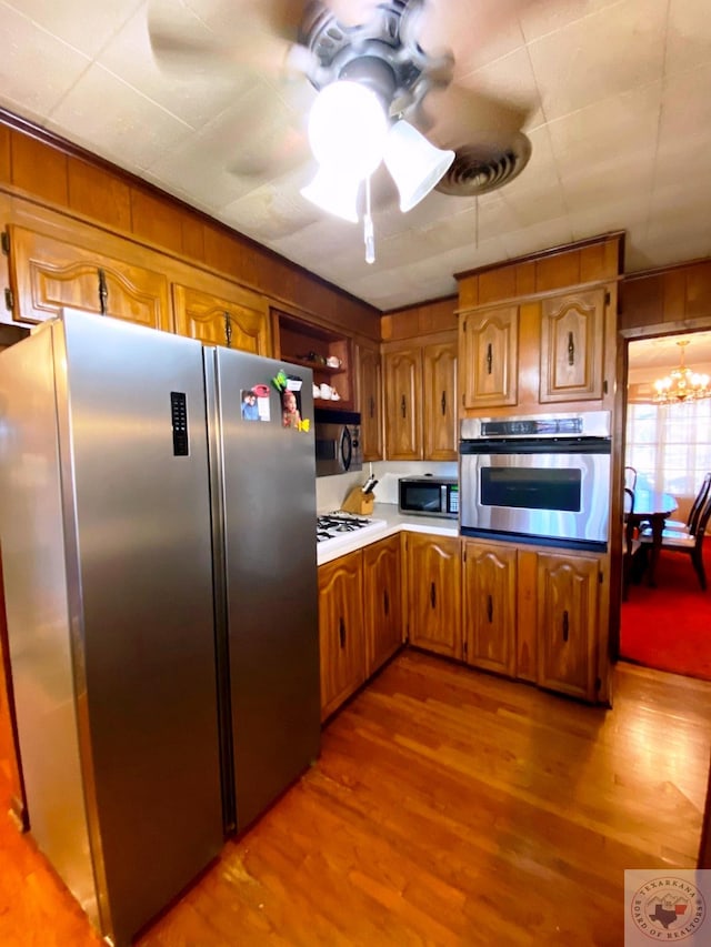 kitchen with ceiling fan with notable chandelier, stainless steel appliances, and light wood-type flooring