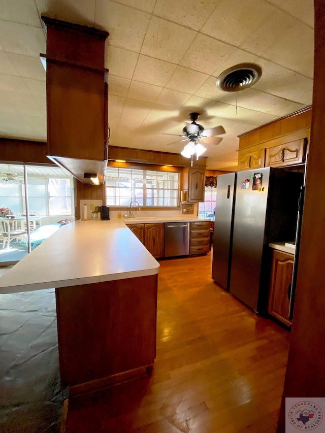 kitchen with hardwood / wood-style floors, appliances with stainless steel finishes, sink, kitchen peninsula, and ceiling fan