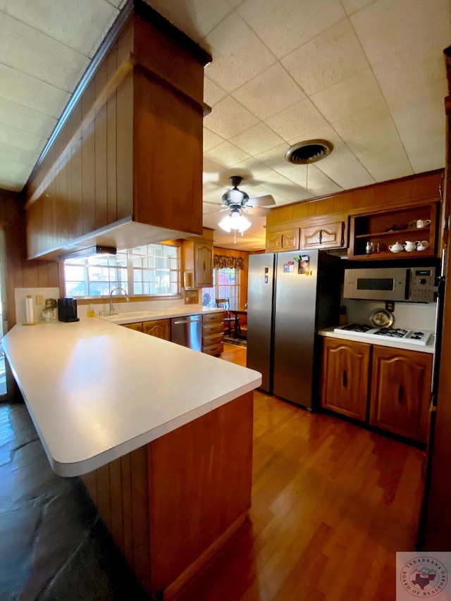 kitchen with appliances with stainless steel finishes, wooden walls, light wood-type flooring, kitchen peninsula, and ceiling fan