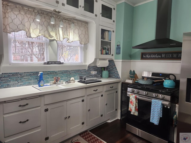 kitchen with decorative backsplash, wall chimney range hood, white cabinets, sink, and stainless steel appliances