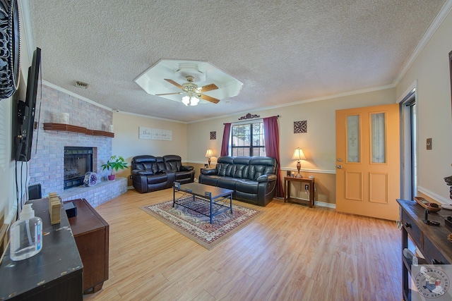 living room featuring a textured ceiling, a fireplace, light wood-type flooring, ceiling fan, and crown molding