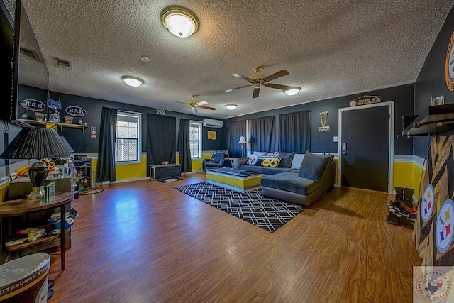 living room featuring a textured ceiling, hardwood / wood-style floors, a wall mounted AC, and ceiling fan