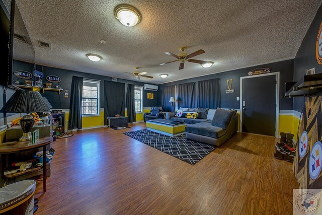 living room with hardwood / wood-style flooring, a textured ceiling, an AC wall unit, and ceiling fan