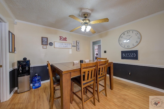 dining space with light hardwood / wood-style floors, a textured ceiling, ornamental molding, and ceiling fan