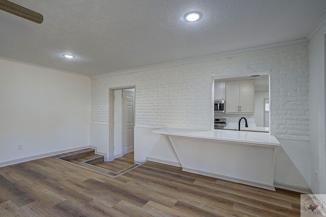 kitchen featuring white cabinetry, crown molding, a textured ceiling, hardwood / wood-style flooring, and stainless steel appliances