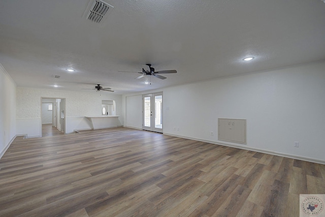 unfurnished living room with brick wall, hardwood / wood-style floors, ornamental molding, a textured ceiling, and french doors