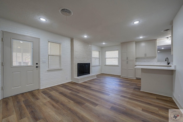 unfurnished living room with brick wall, a fireplace, sink, dark hardwood / wood-style flooring, and a textured ceiling