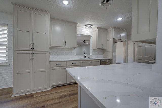 kitchen featuring sink, light stone counters, light hardwood / wood-style flooring, stainless steel dishwasher, and white cabinets