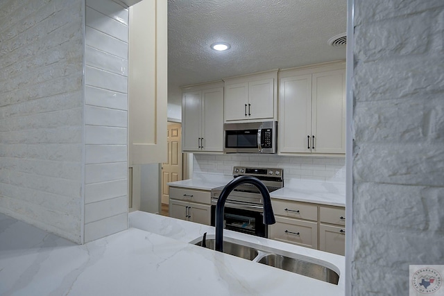 kitchen with light stone countertops, appliances with stainless steel finishes, white cabinetry, sink, and backsplash