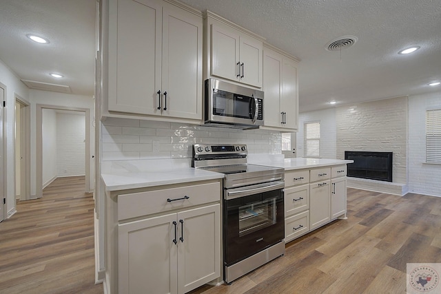 kitchen with stainless steel appliances, a large fireplace, white cabinets, and light hardwood / wood-style flooring