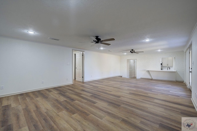 unfurnished living room with sink, hardwood / wood-style floors, ceiling fan, and ornamental molding