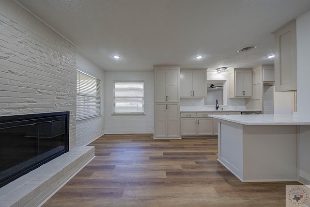 kitchen featuring sink, backsplash, white cabinets, dark hardwood / wood-style flooring, and a brick fireplace