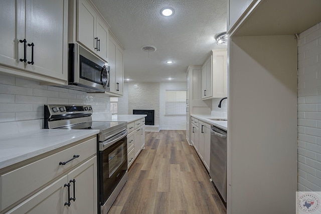 kitchen featuring appliances with stainless steel finishes, sink, white cabinets, and light wood-type flooring