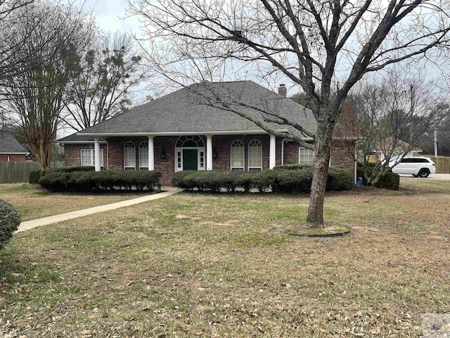 view of front of property featuring a shingled roof, a chimney, a front lawn, and brick siding