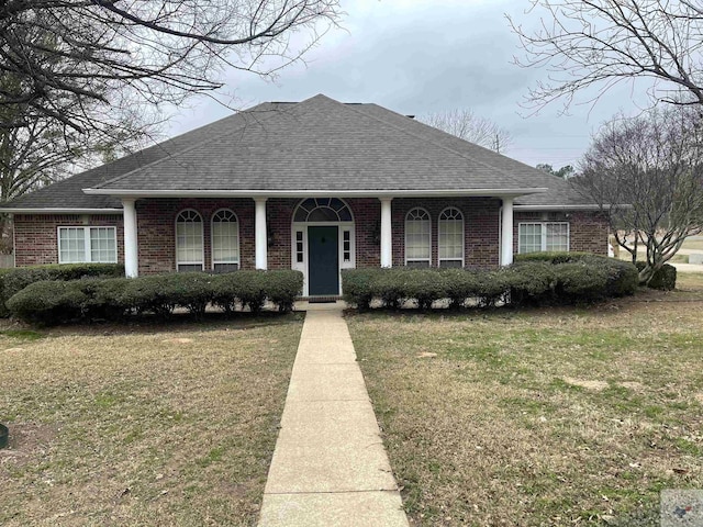 view of front of property featuring roof with shingles, brick siding, and a front lawn