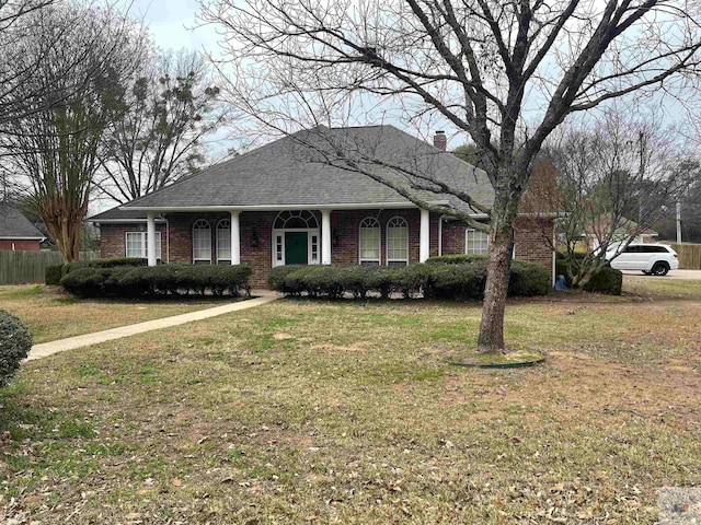 ranch-style home featuring roof with shingles, a front yard, brick siding, and a chimney