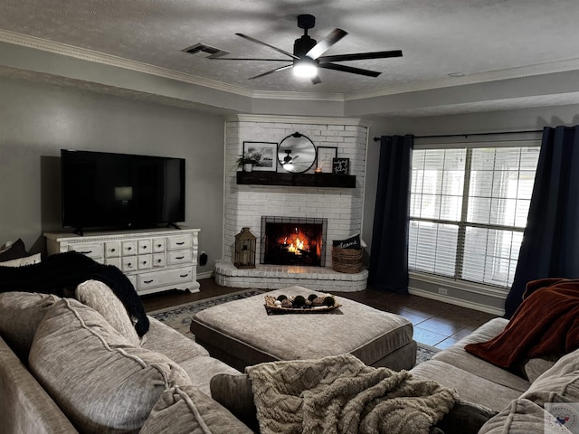 living room featuring a fireplace, dark tile patterned floors, ceiling fan, crown molding, and a textured ceiling