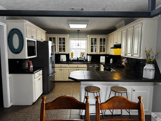 kitchen with kitchen peninsula, hanging light fixtures, sink, range, and fridge with ice dispenser