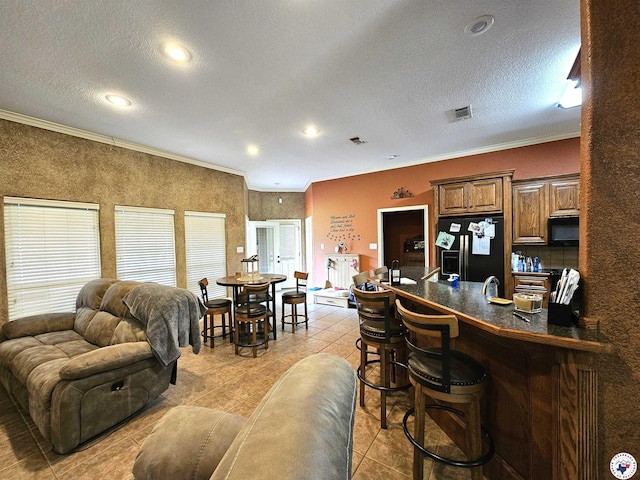 interior space with a breakfast bar area, light tile patterned floors, black appliances, a peninsula, and ornamental molding