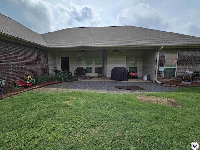 rear view of property featuring ceiling fan, roof with shingles, a patio area, brick siding, and a yard