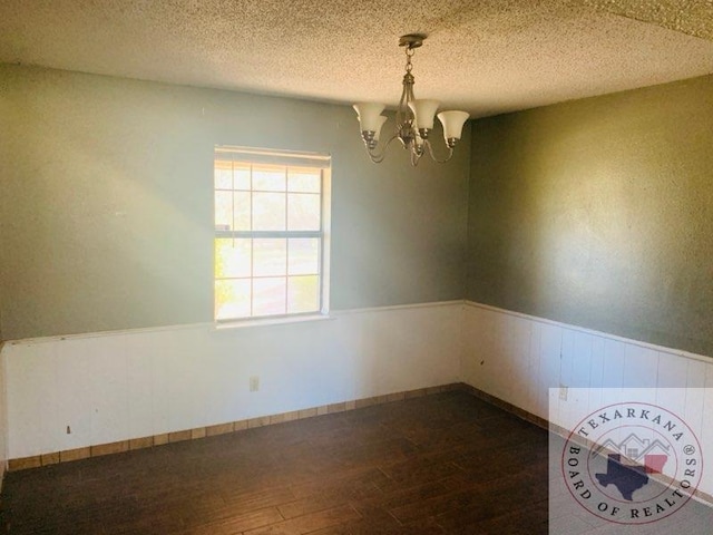 spare room featuring an inviting chandelier, dark hardwood / wood-style flooring, and a textured ceiling