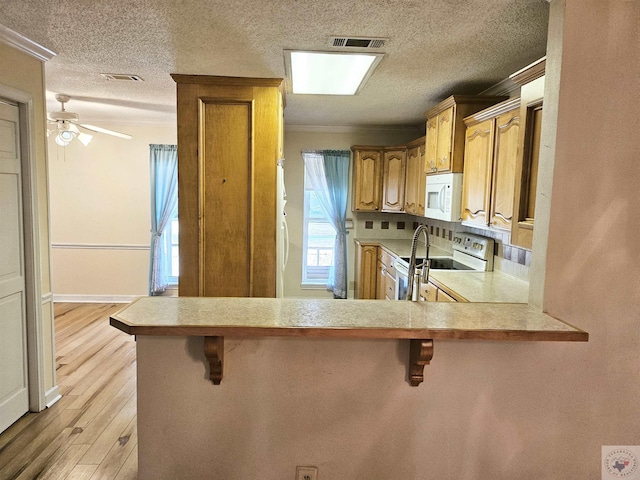 kitchen featuring crown molding, white appliances, light hardwood / wood-style flooring, a kitchen bar, and kitchen peninsula