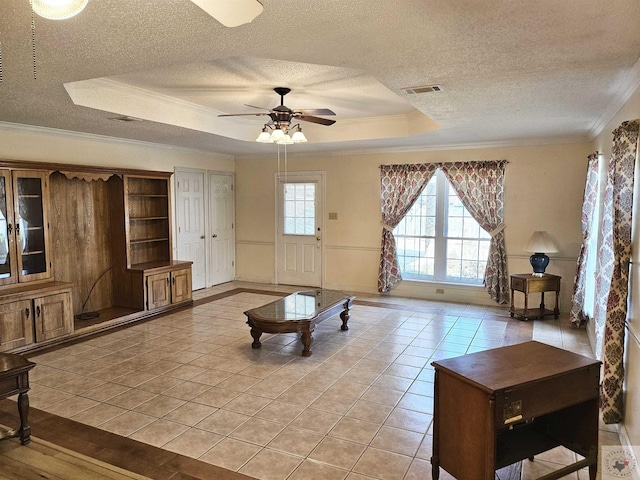 living room featuring light tile patterned floors, a textured ceiling, a tray ceiling, and crown molding