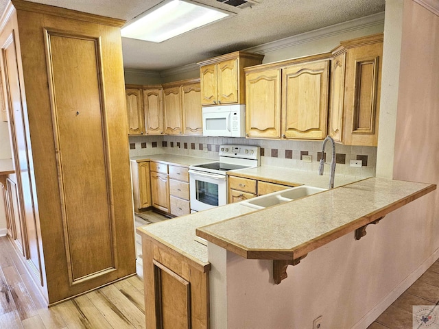 kitchen featuring crown molding, white appliances, a breakfast bar, and kitchen peninsula