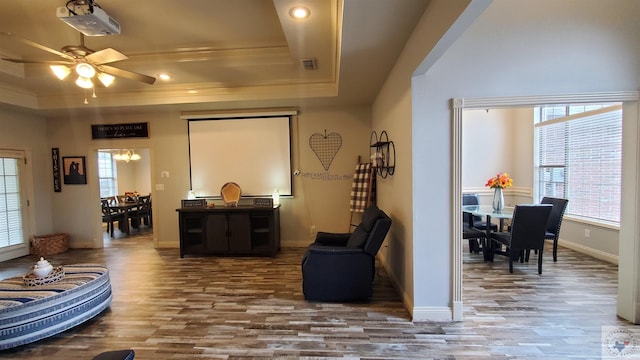 living room featuring a raised ceiling, ornamental molding, hardwood / wood-style flooring, and ceiling fan with notable chandelier