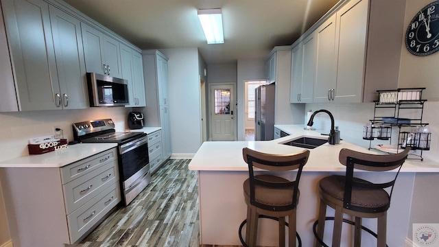 kitchen featuring a kitchen bar, sink, tasteful backsplash, hardwood / wood-style flooring, and stainless steel appliances
