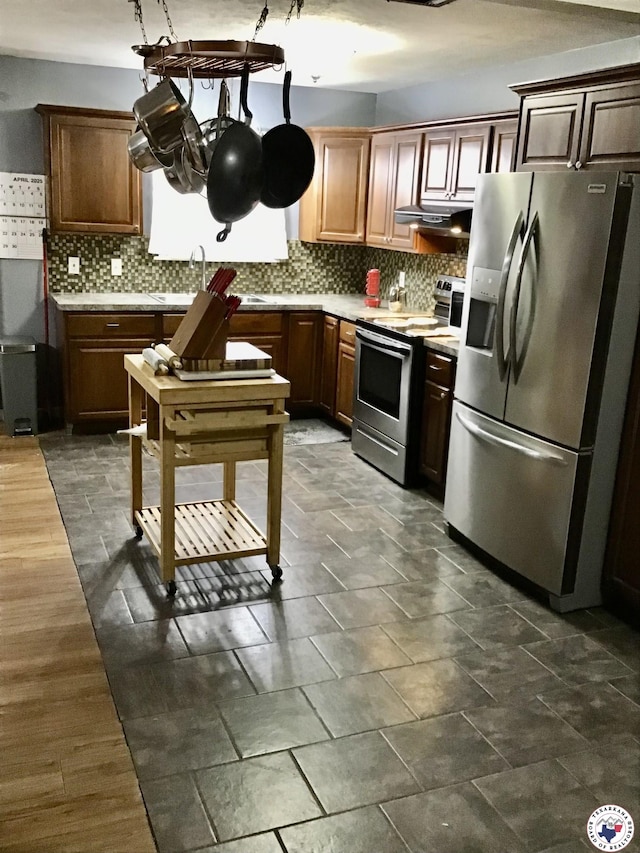 kitchen featuring decorative backsplash, light countertops, under cabinet range hood, and appliances with stainless steel finishes