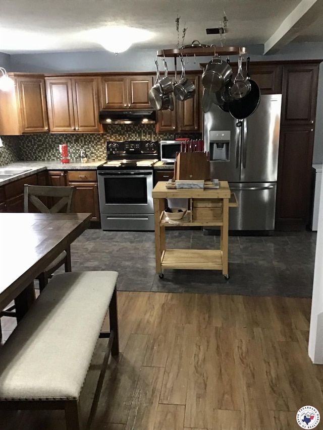 kitchen with tasteful backsplash, stainless steel appliances, light countertops, under cabinet range hood, and dark wood-type flooring