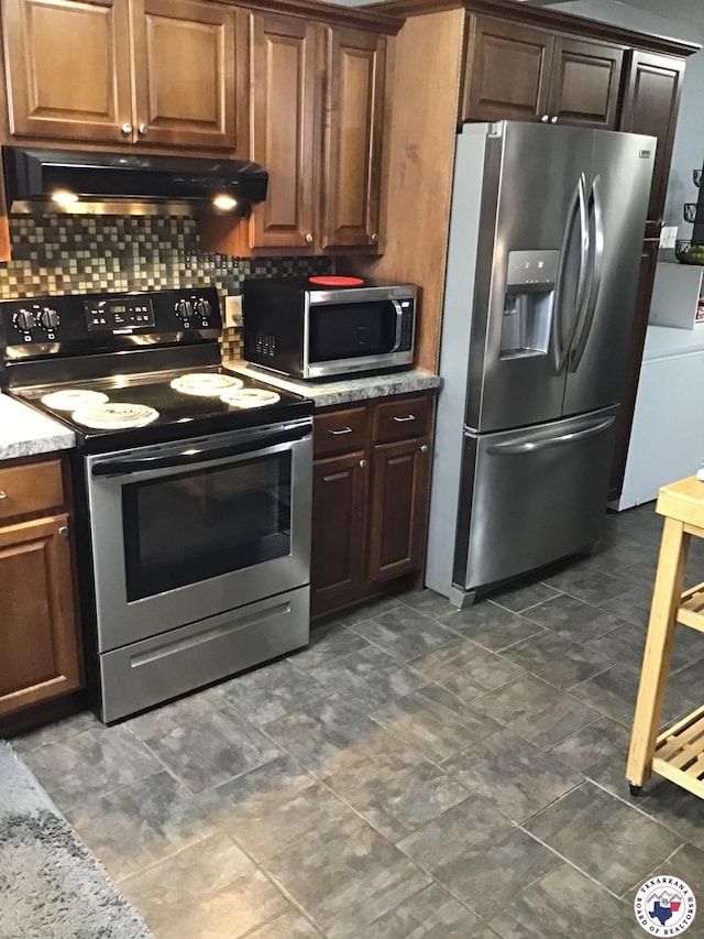 kitchen featuring under cabinet range hood, appliances with stainless steel finishes, tasteful backsplash, and light stone counters