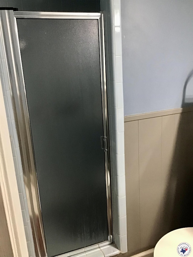 full bathroom with a shower stall and a wainscoted wall