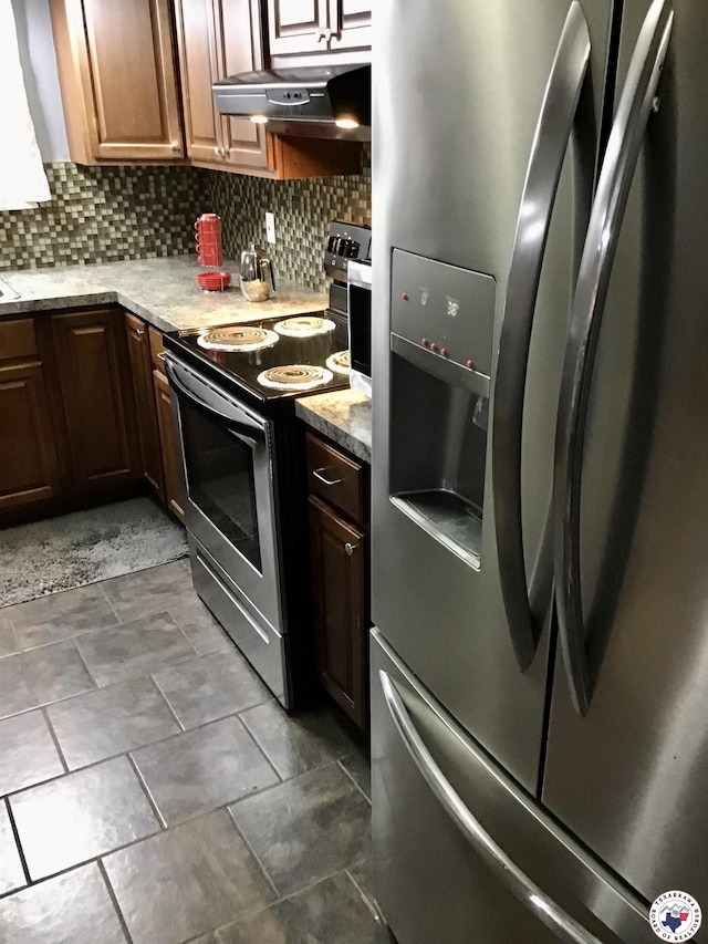 kitchen with decorative backsplash, under cabinet range hood, stainless steel appliances, and dark tile patterned flooring