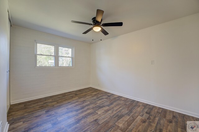 spare room with dark wood-type flooring, brick wall, and ceiling fan