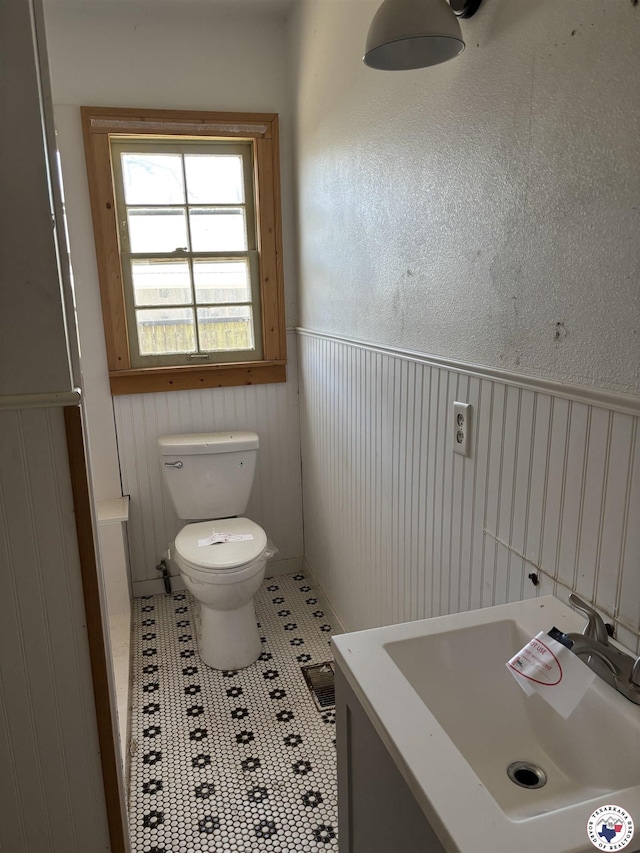 1100 W Jackson St, Clarksville, TX 75426 - half bath featuring a sink, toilet, a wainscoted wall, and tile patterned floors
