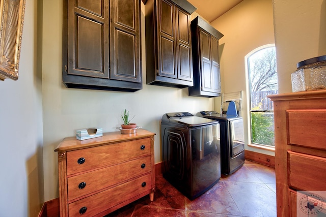 clothes washing area with washing machine and dryer, dark tile patterned floors, and cabinets