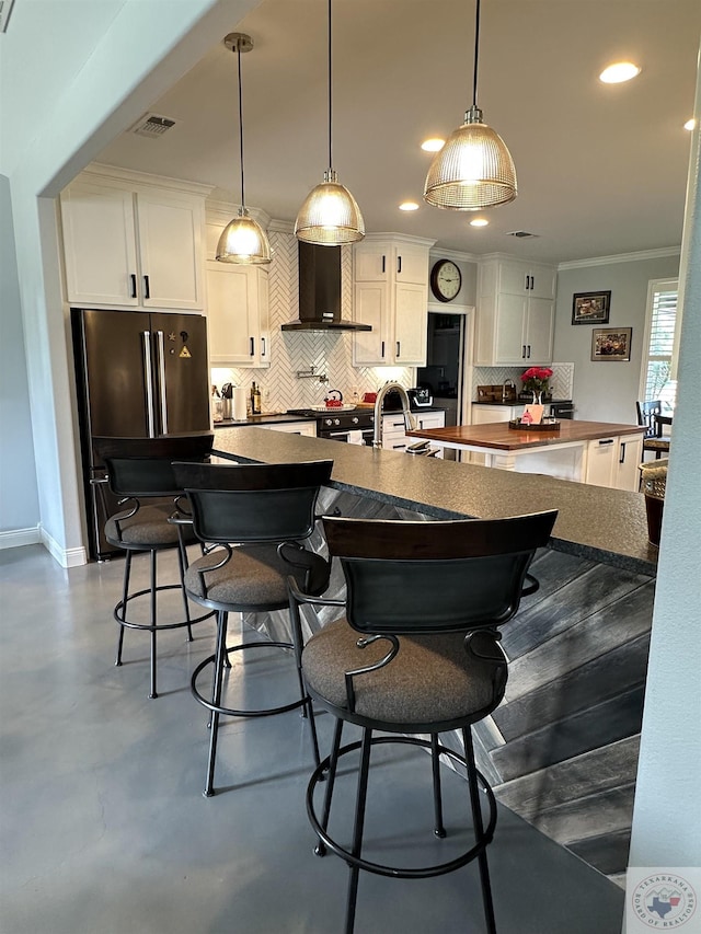 kitchen featuring concrete floors, white cabinetry, wall chimney range hood, and high quality fridge