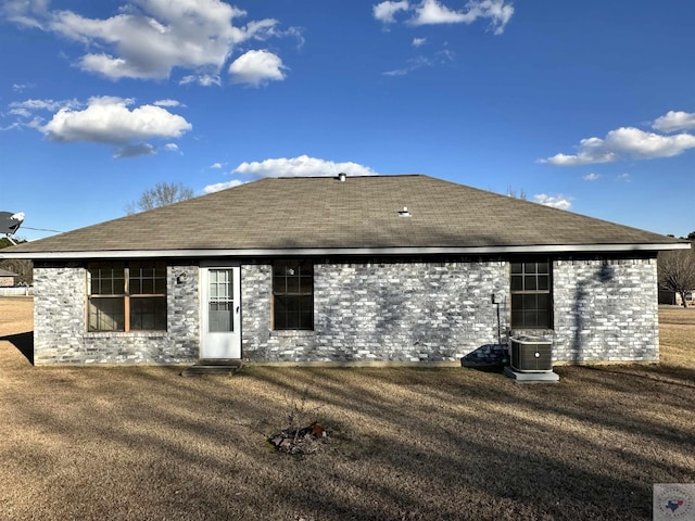 rear view of house with central AC unit and a lawn