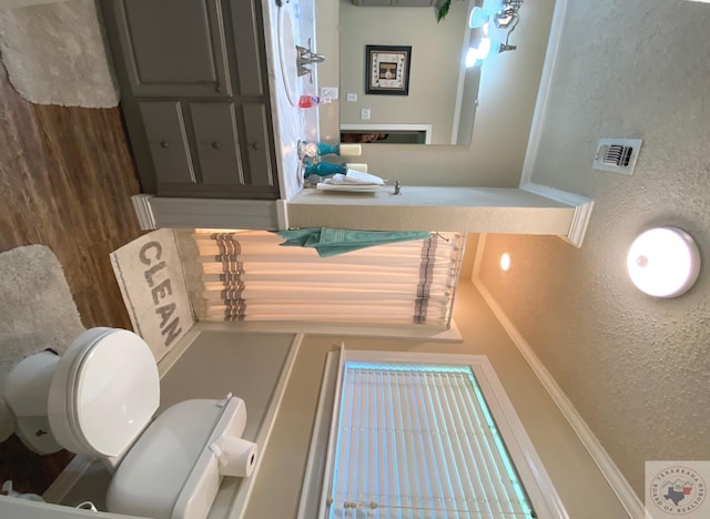 bathroom featuring toilet, visible vents, and a textured wall