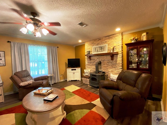 living area with visible vents, ceiling fan, dark wood-type flooring, a wood stove, and a textured ceiling