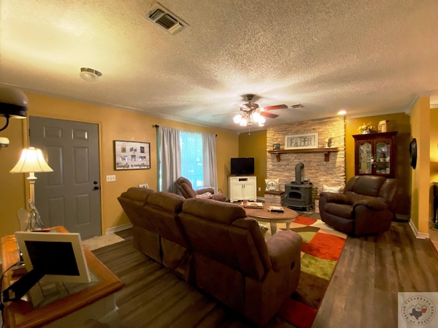 living area with visible vents, ceiling fan, wood finished floors, a wood stove, and a textured ceiling