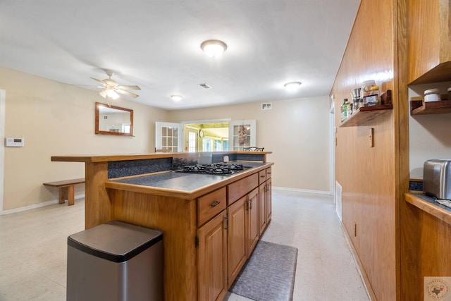 kitchen with a kitchen bar, stainless steel gas cooktop, and ceiling fan