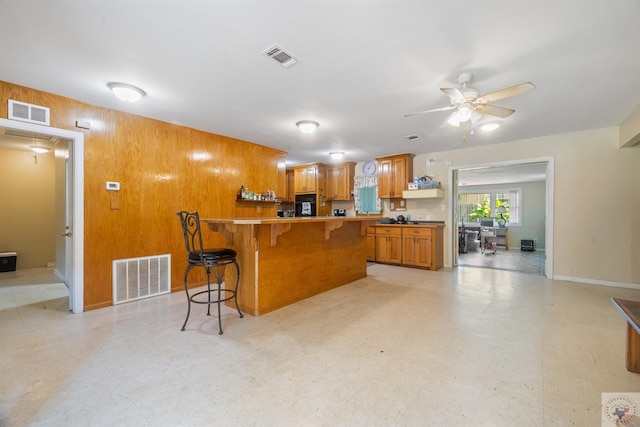 kitchen with a kitchen bar, kitchen peninsula, ceiling fan, and wooden walls