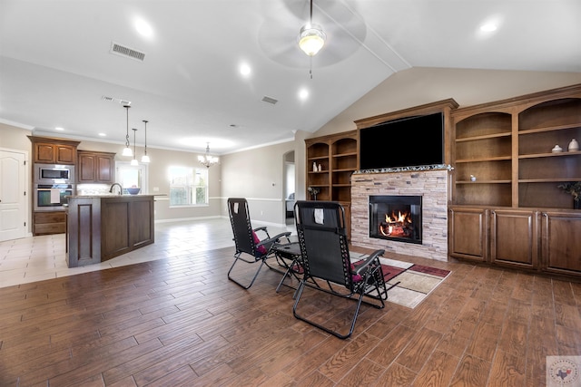 living room featuring hardwood / wood-style flooring, sink, a stone fireplace, and vaulted ceiling