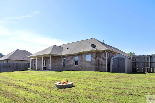 back of property featuring a storage shed, a fire pit, and a lawn