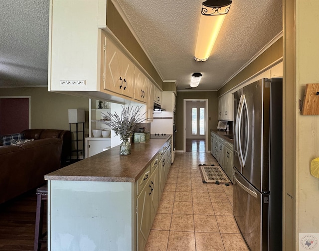 kitchen with stainless steel refrigerator, ornamental molding, light tile patterned floors, and a textured ceiling