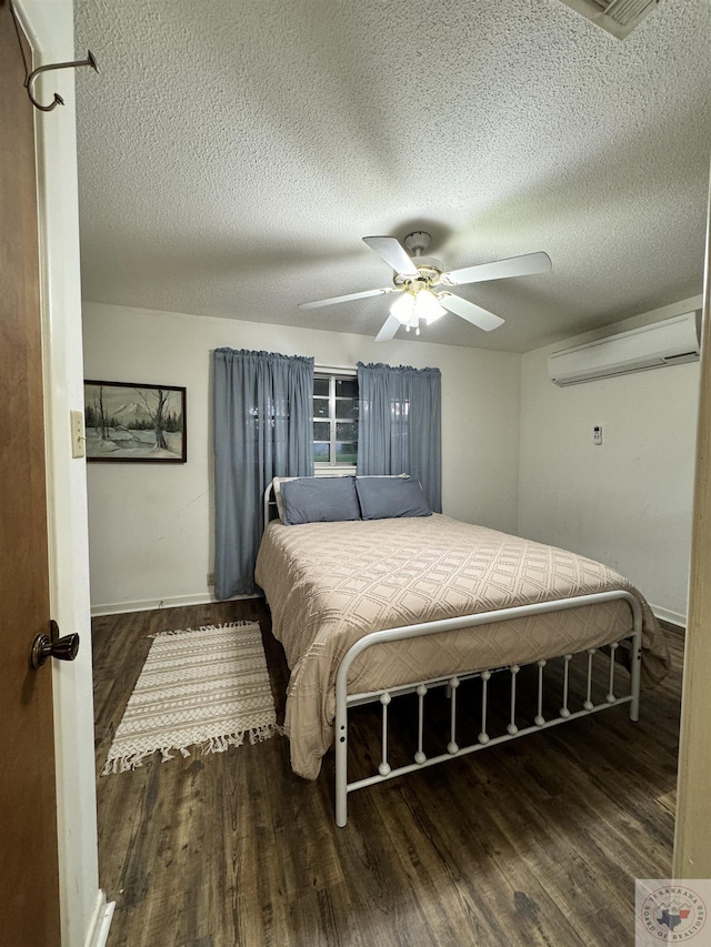 bedroom featuring a textured ceiling, a wall mounted AC, dark hardwood / wood-style floors, and ceiling fan